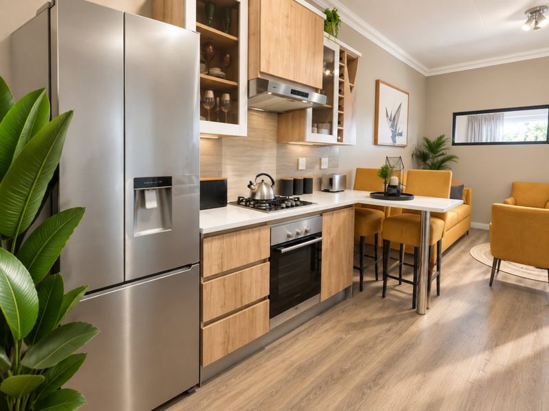 Modern open-plan kitchen featuring light wood cabinetry, stone countertops, integrated appliances, and a breakfast bar, seamlessly flowing into the living area.