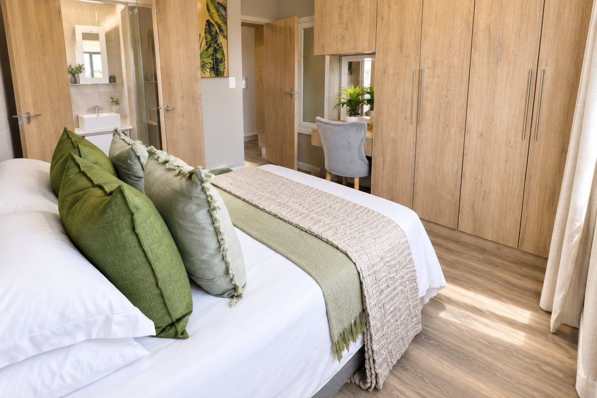 A well-appointed bedroom featuring extensive built-in wooden cabinetry, integrated vanity, laminate flooring, and direct access to an en-suite bathroom.
