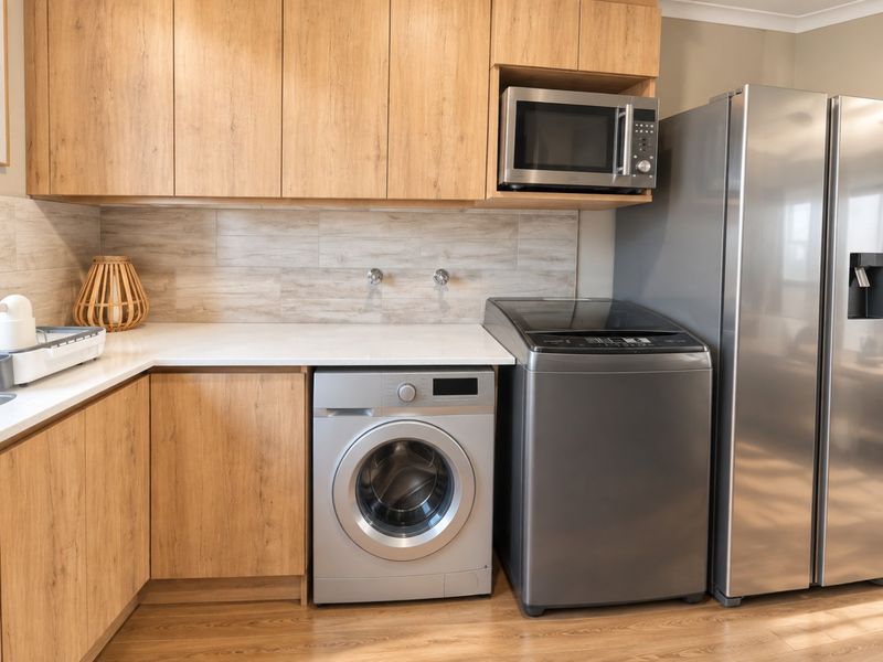A modern, well-maintained laundry area featuring wood-finish cabinetry, stone countertops, tiled backsplash, and dedicated space for laundry appliances.