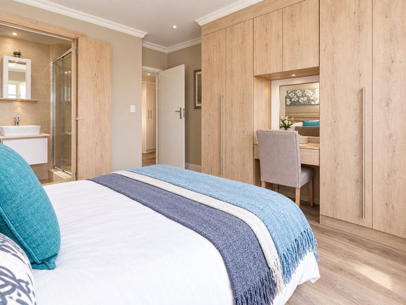 Well-appointed bedroom featuring extensive built-in cabinetry with an integrated vanity and a modern en-suite bathroom with a glass shower enclosure.