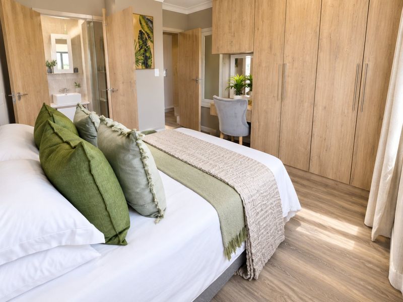 A well-appointed bedroom featuring extensive built-in wooden cabinetry, laminate flooring, and an integrated en-suite bathroom with a modern vanity.