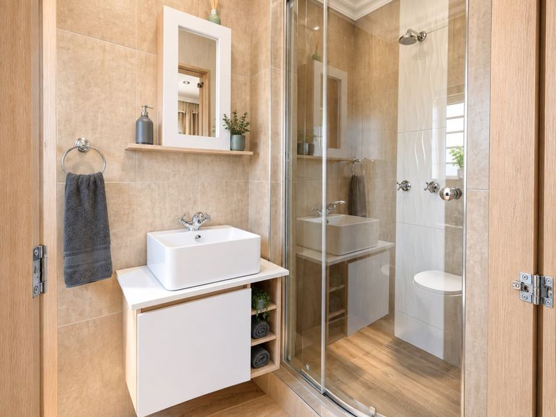 Modern bathroom featuring a vessel sink on a wall-mounted vanity, a glass-enclosed shower, and neutral-toned wall and floor tiling.