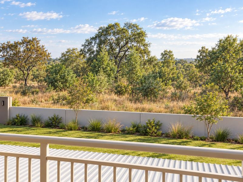 A scenic view from a balcony overlooking a well-maintained garden, boundary wall, and natural bushveld landscape.