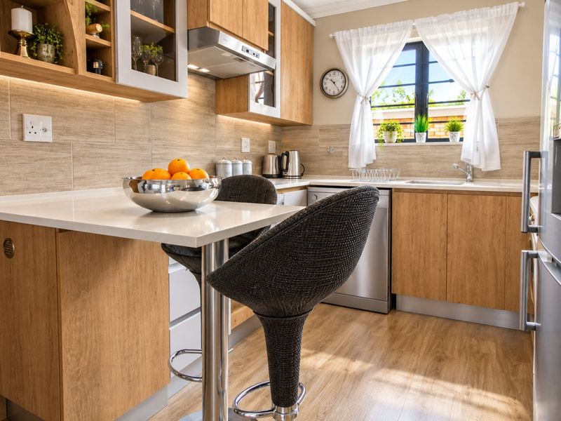 Modern kitchen featuring light wood cabinetry, stone countertops, integrated extractor fan, and a breakfast bar, complemented by warm under-cabinet lighting and natural light.