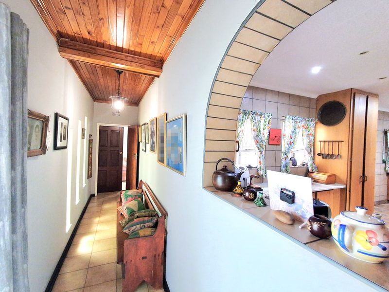 A hallway featuring a timber-clad ceiling and tiled flooring, with an arched opening providing a view into the adjacent kitchen area.