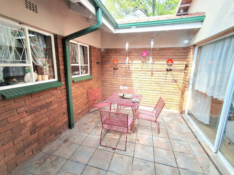 A covered outdoor patio area featuring exposed brick walls, tiled flooring, and direct access to the interior via a sliding glass door.
