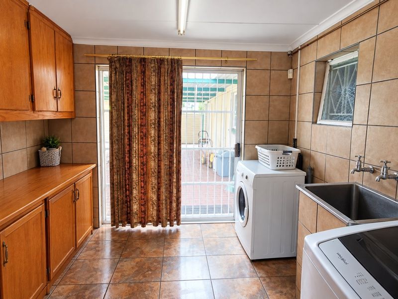 Functional laundry room featuring built-in wooden cabinetry, tiled finishes, a stainless steel sink, and direct access to the rear outdoor area.