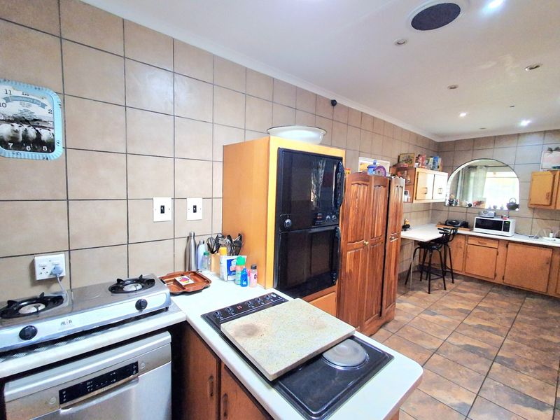 Spacious kitchen featuring extensive tiled splashbacks, built-in cabinetry, dual cooking hobs, and a built-in oven, offering a functional layout with ample storage.