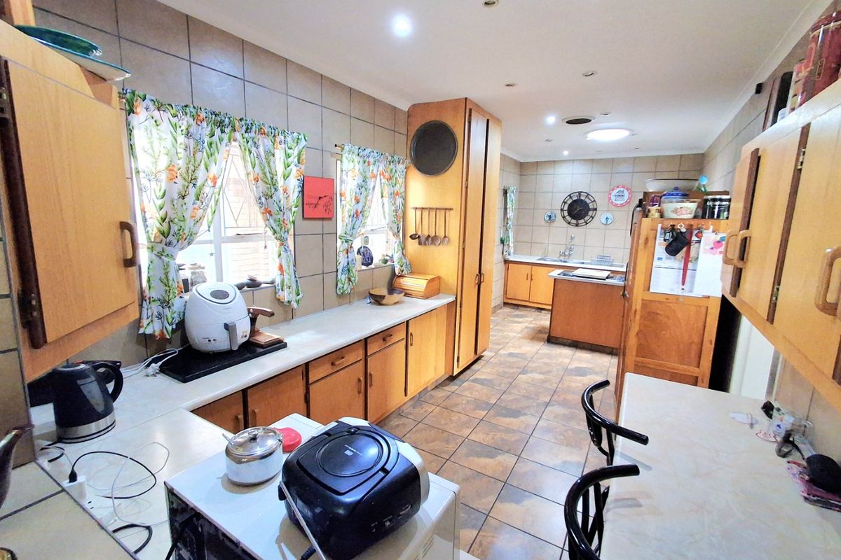 A spacious kitchen featuring extensive wooden cabinetry, tiled flooring, and a tiled backsplash, offering a functional layout with ample counter space.