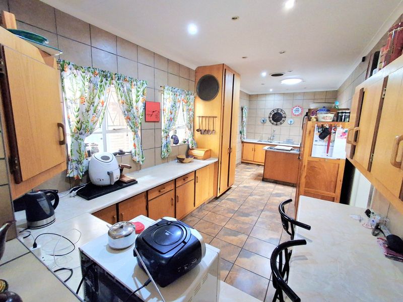 A spacious kitchen featuring extensive wooden cabinetry, tiled flooring, and a tiled backsplash, offering a functional layout with ample counter space.