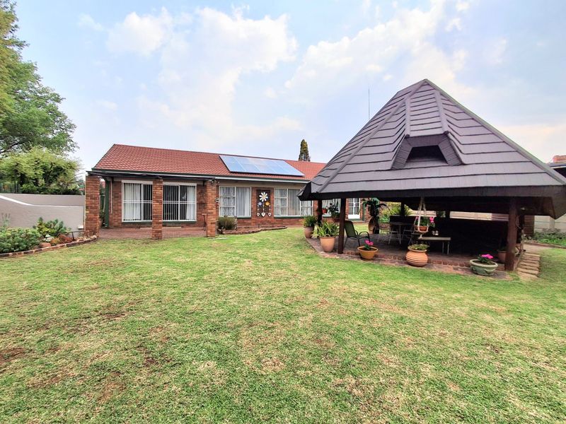 Rear view of the house featuring a brick facade, solar panels, a well-maintained lawn, and a large covered gazebo area.