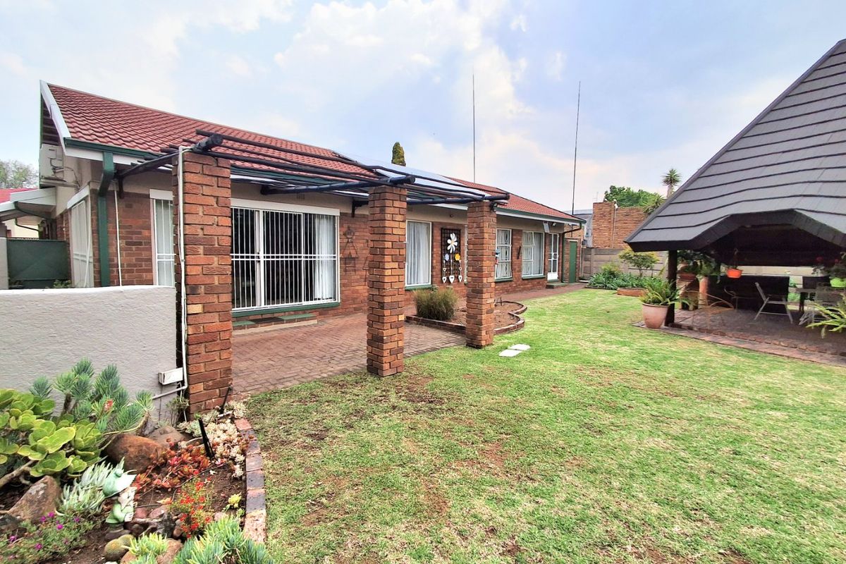 Rear view of the property featuring a brick facade, paved patio area with brick pillars, a well-maintained garden, and a separate thatched gazebo.