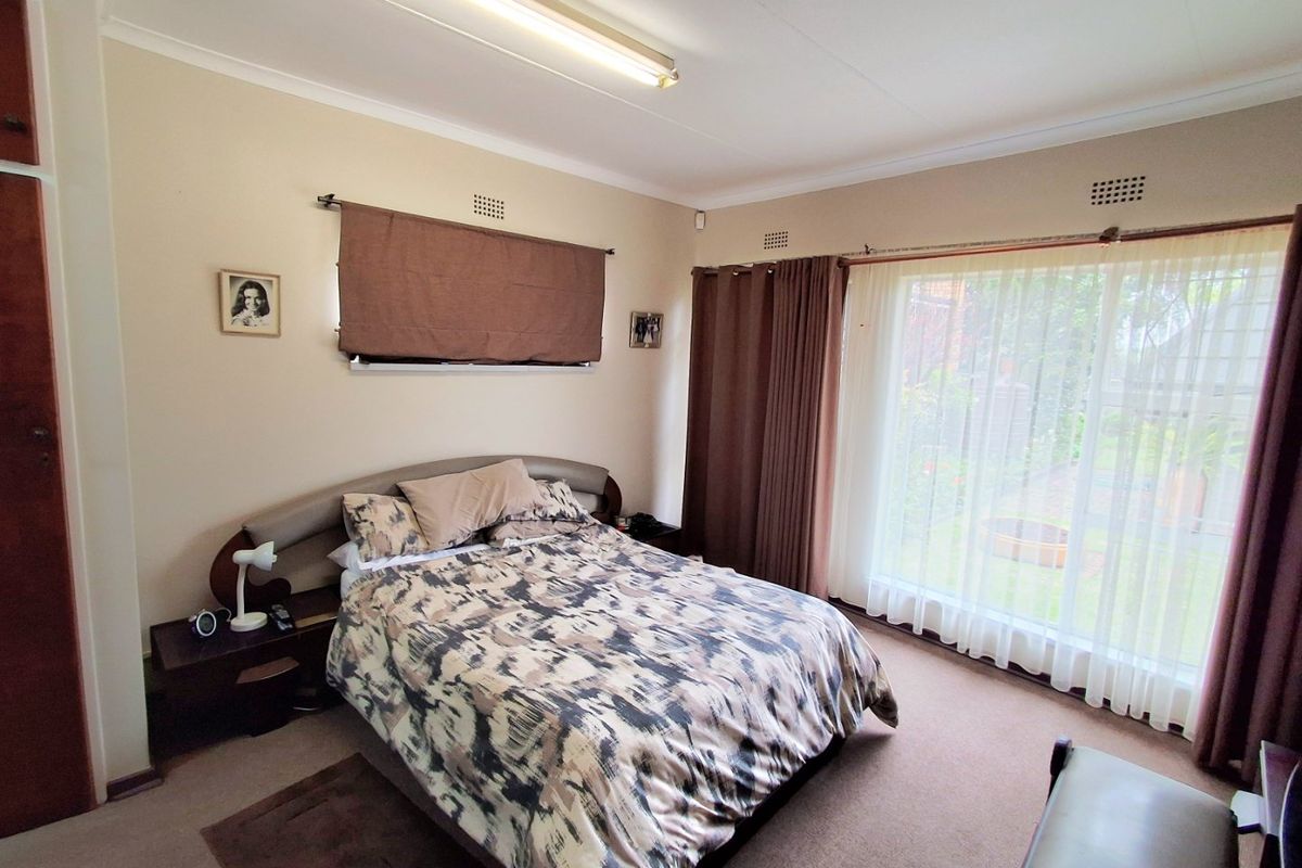 A spacious bedroom featuring built-in cupboards, large windows with garden views, and neutral wall finishes, offering a comfortable and functional living space.