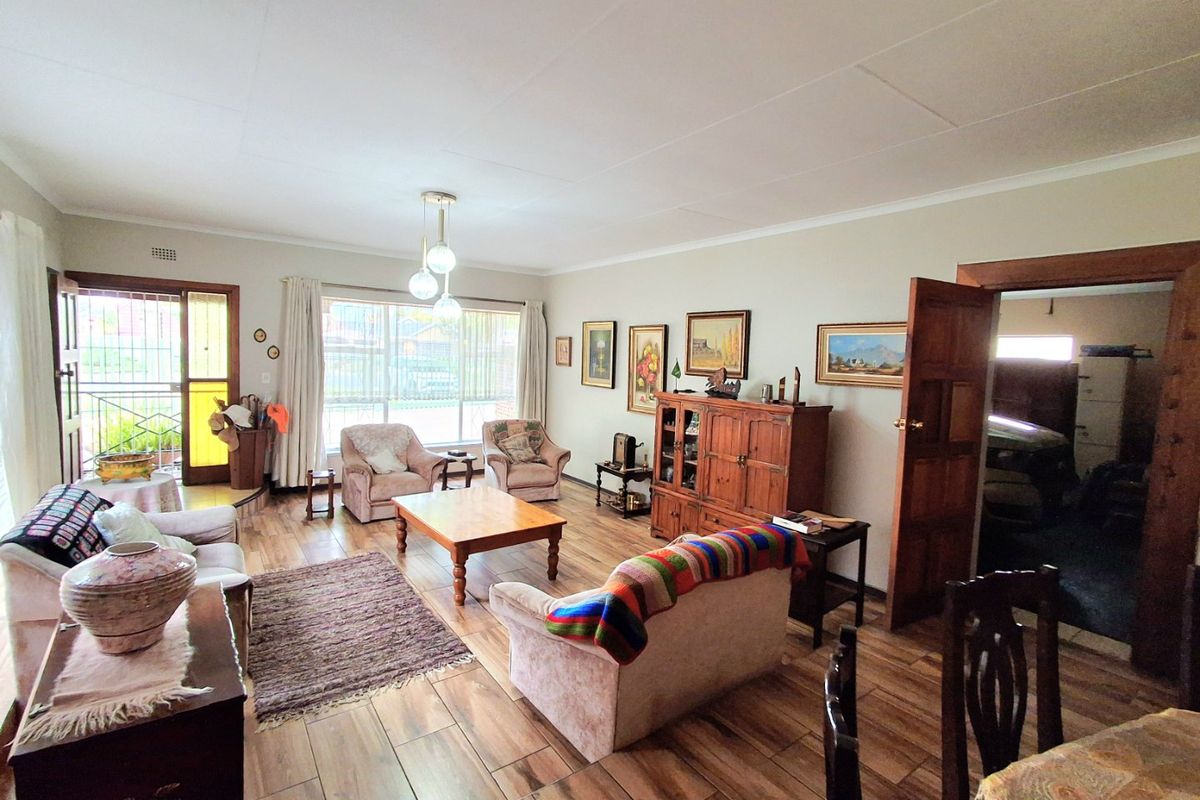 Spacious living room featuring wood-look tiled flooring, large windows for natural light, and direct access to an exterior security gate.