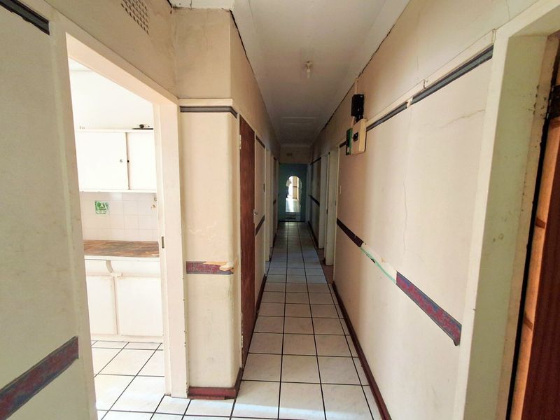 A long, tiled hallway providing access to multiple rooms, featuring dated wall finishes and visible signs of wear requiring maintenance or renovation.