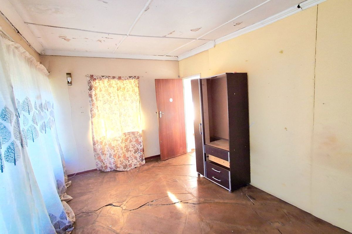 A bedroom featuring tiled flooring with significant cracking and a ceiling in need of repair, offering a blank canvas for renovation.