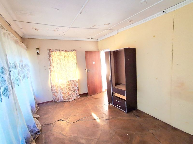 A bedroom featuring tiled flooring with significant cracking and a ceiling in need of repair, offering a blank canvas for renovation.