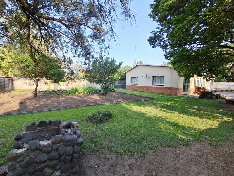 A spacious rear garden featuring a stone-built braai area, established lawn, and mature trees, providing a private outdoor space.