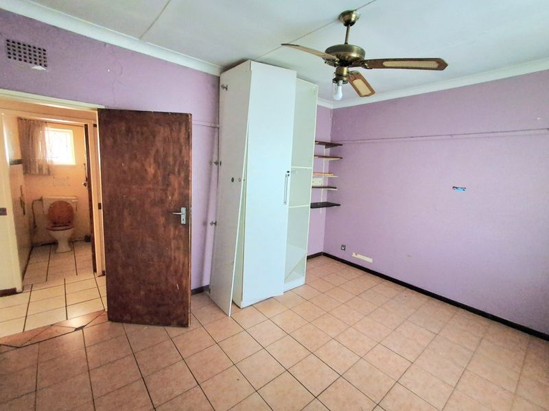 A bedroom featuring tiled flooring, a ceiling fan, and built-in shelving, with an adjacent bathroom visible through the doorway.