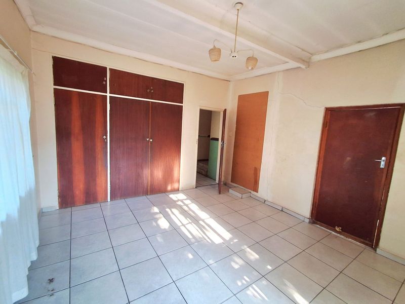 An empty bedroom featuring tiled flooring, built-in wooden cupboards, and a ceiling light fixture, requiring some cosmetic updates to the walls and finishes.