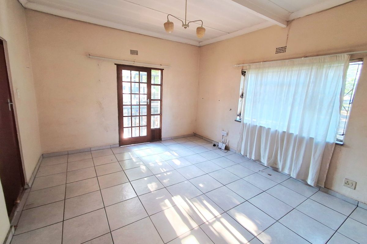 An empty living room featuring tiled flooring, exposed beam ceilings, and a timber-framed glass door leading to the exterior.
