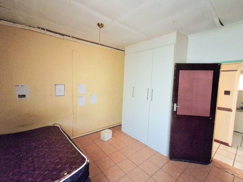 A bedroom featuring tiled flooring and a built-in wardrobe, currently requiring cosmetic updates and wall repairs to improve its overall condition.