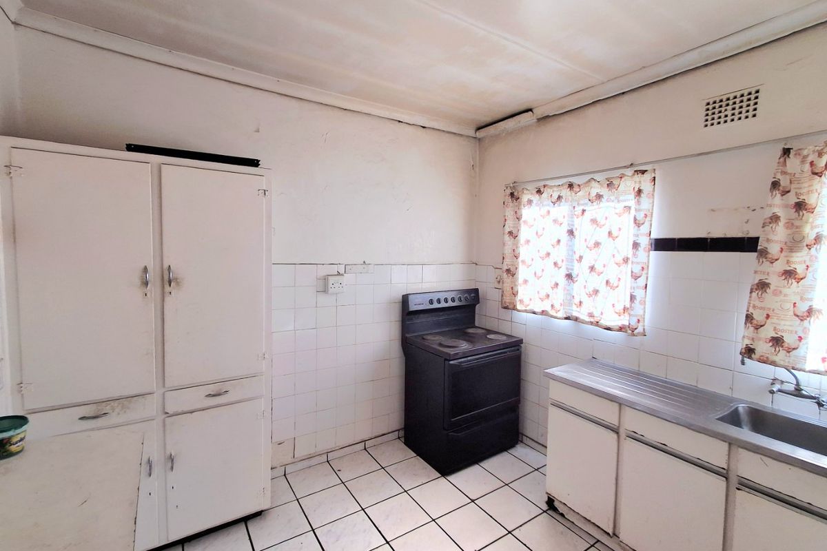 A dated kitchen featuring original cabinetry, a stainless steel sink, and a freestanding stove, requiring renovation to modernize the space.
