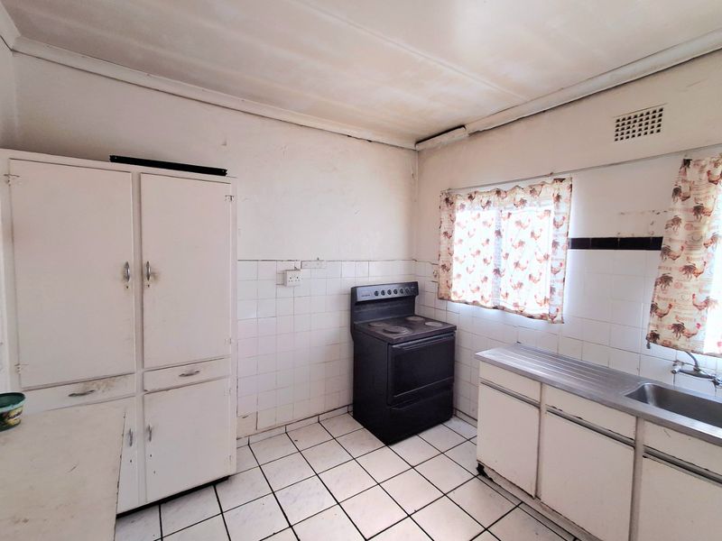 A dated kitchen featuring original cabinetry, a stainless steel sink, and a freestanding stove, requiring renovation to modernize the space.