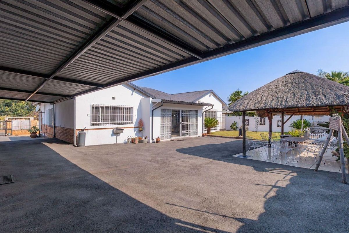 Spacious rear exterior featuring a large paved driveway, a covered carport, and a traditional thatched lapa, ideal for outdoor entertaining.