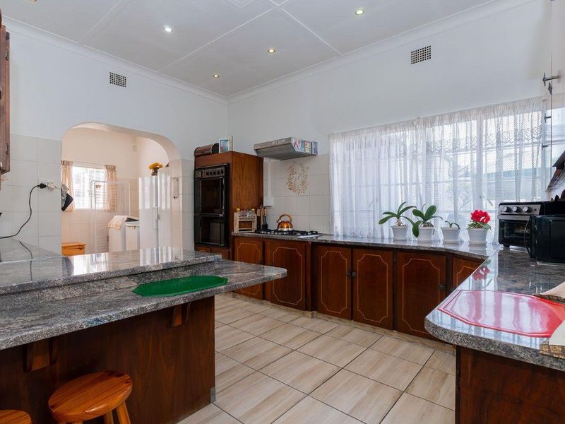 A functional kitchen featuring granite countertops, built-in oven, gas hob, and tiled flooring, with an open archway leading to an adjacent utility area.