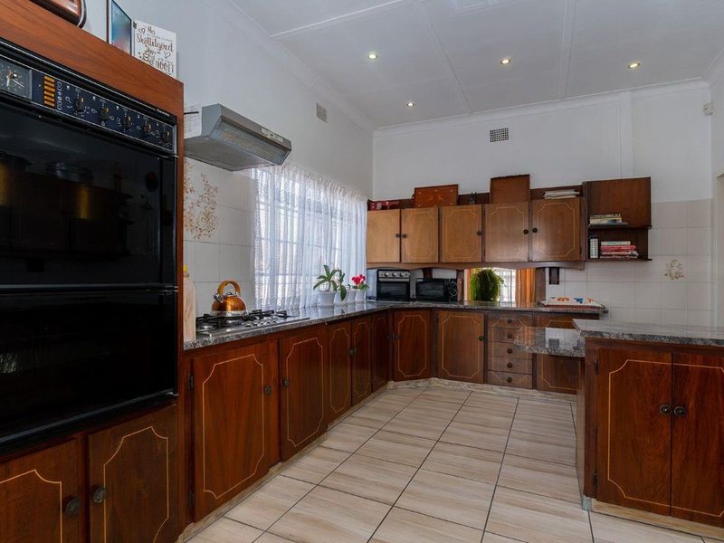 A functional kitchen featuring traditional wooden cabinetry, granite countertops, a built-in double oven, and a gas hob with an extractor fan.