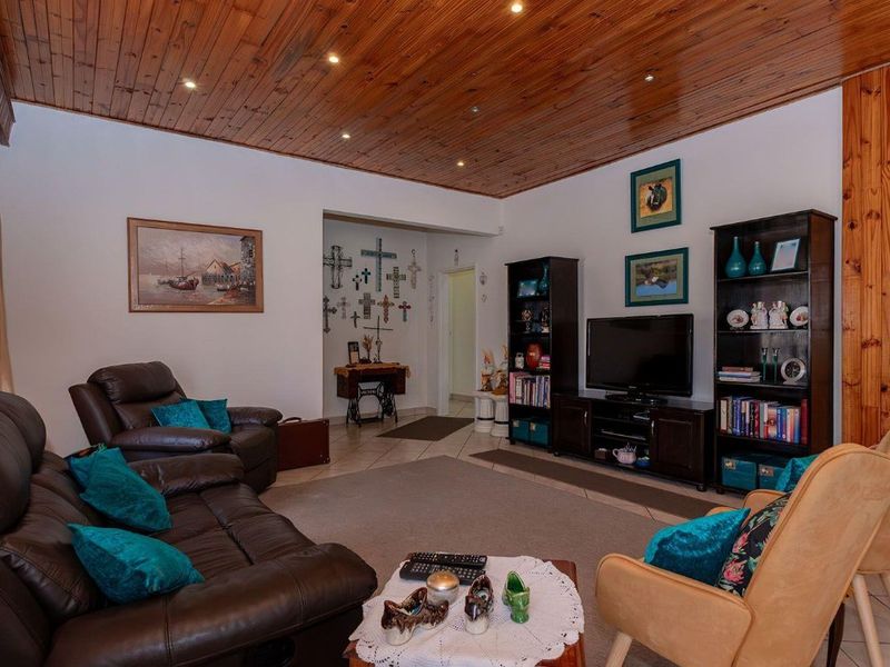A comfortable living room featuring a distinctive timber-clad ceiling with recessed downlights and neutral tiled flooring throughout.