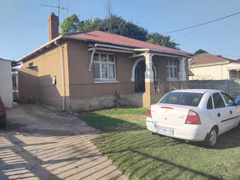 Front elevation of a single-story house featuring a covered porch with decorative columns, a corrugated metal roof, and a concrete driveway.
