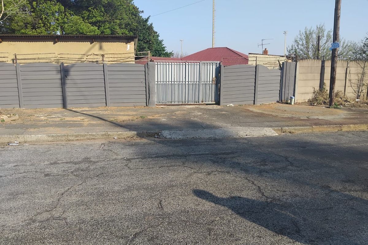 Front exterior view showing a gated entrance with a precast concrete boundary wall and paved driveway access from the street.