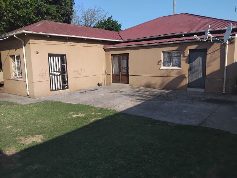 Rear exterior view of the house featuring a concrete patio area, corrugated metal roofing, and security gates on doors and windows.