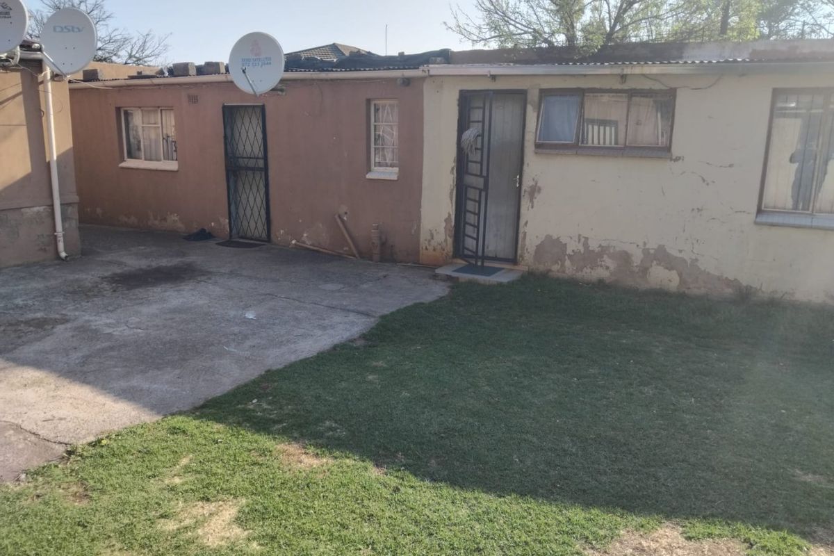 Rear exterior view of the property featuring a concrete patio area, lawn, and building facade with security gates and satellite dishes.