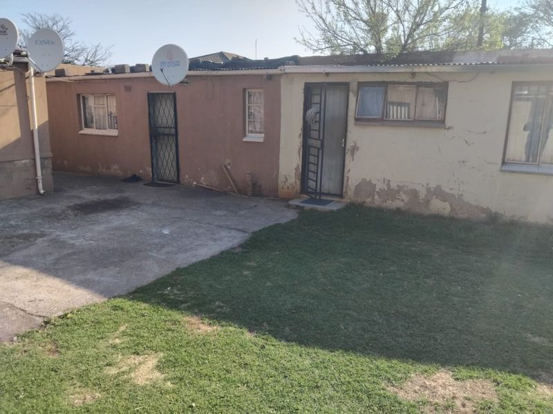 Rear exterior view of the property featuring a concrete patio area, lawn, and building facade with security gates and satellite dishes.