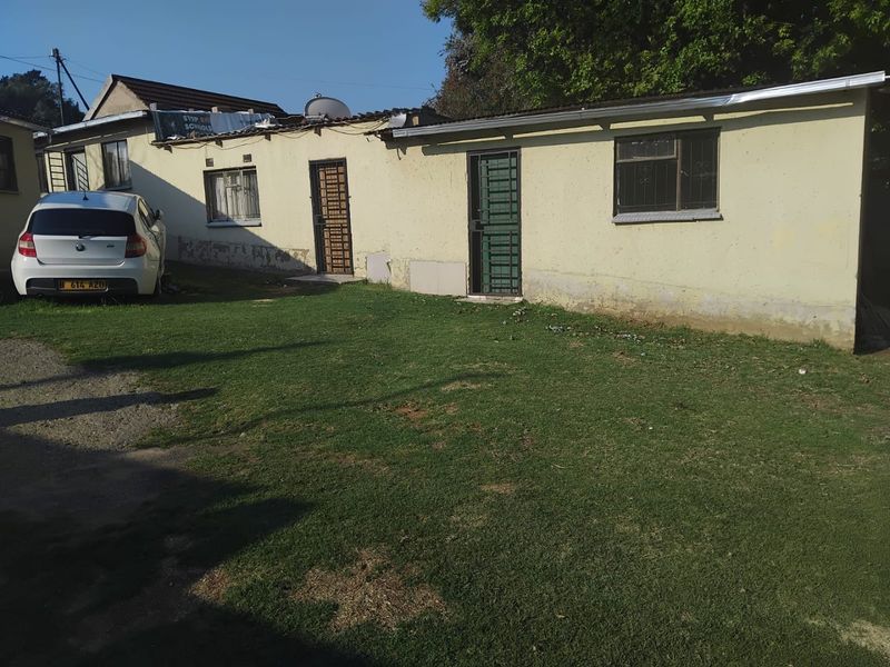 Rear exterior view of a single-story house featuring a lawn area, security gates, and visible signs of exterior wall and roof maintenance requirements.
