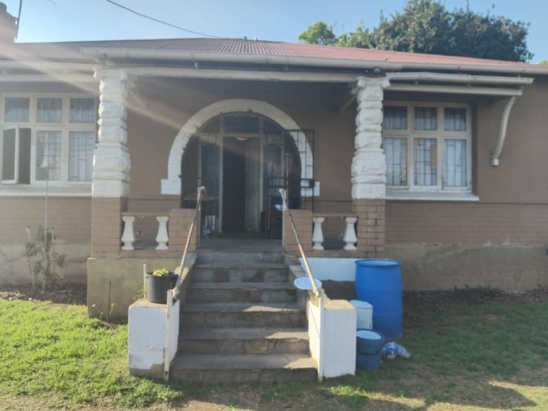Front elevation of a traditional house featuring a covered porch, stone columns, arched entrance, and concrete steps leading to the main door.