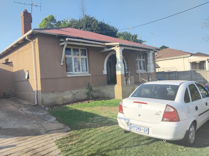Front elevation of a single-story house featuring a covered porch with decorative columns, a corrugated metal roof, and a concrete driveway.