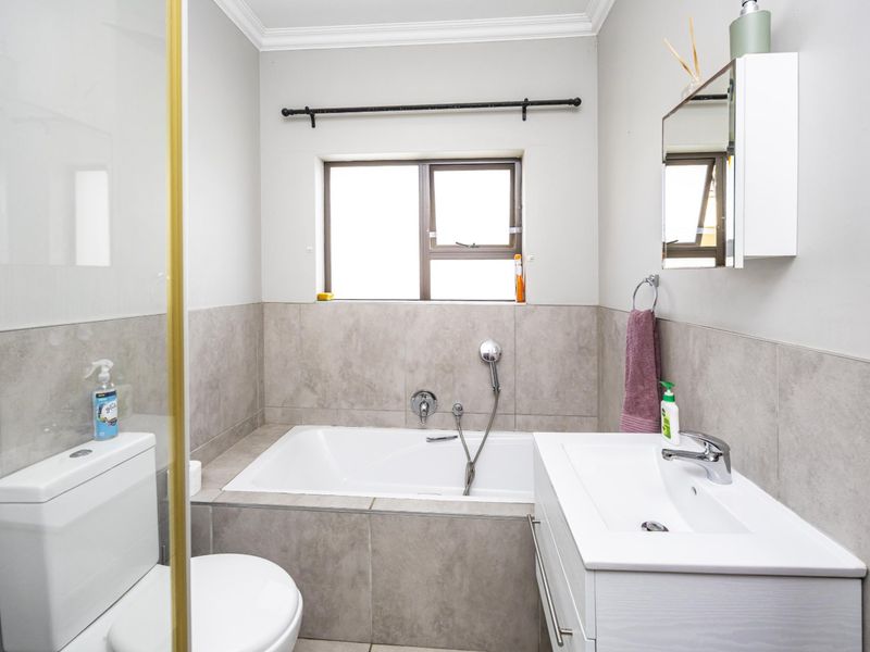 A modern bathroom featuring a built-in bathtub, vanity with basin, toilet, and neutral wall tiling.