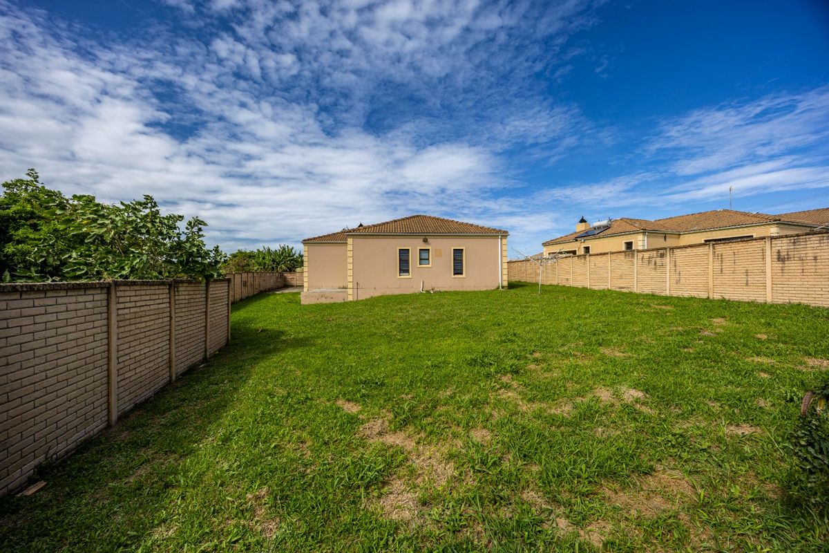 A spacious rear garden featuring a large lawn area enclosed by perimeter brick boundary walls and a view of the rear building elevation.