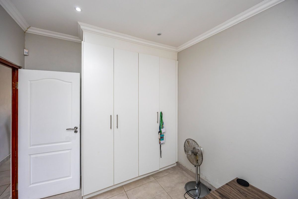 A bedroom featuring neutral walls, tiled flooring, and white built-in cupboards with modern hardware.