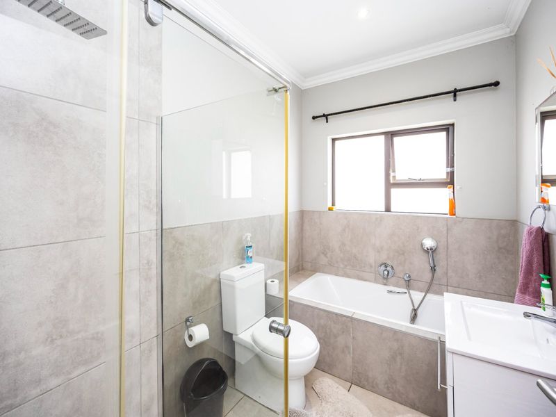 Modern bathroom featuring a walk-in shower with glass screen, built-in bathtub, toilet, and vanity basin with neutral tiled finishes.