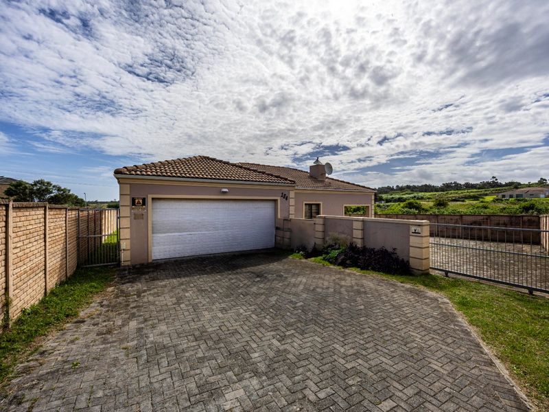 Front view of the property featuring a paved driveway, double garage, and secure perimeter wall with metal gate access.