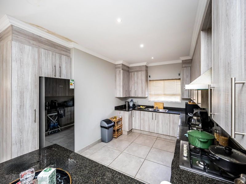 Modern kitchen featuring light wood-grain cabinetry, dark granite countertops, a gas hob with extractor fan, and tiled flooring.