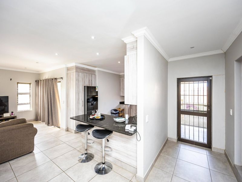 Open-plan living area featuring a kitchen with a granite breakfast bar, tiled flooring, recessed lighting, and direct access to the exterior via a security gate.