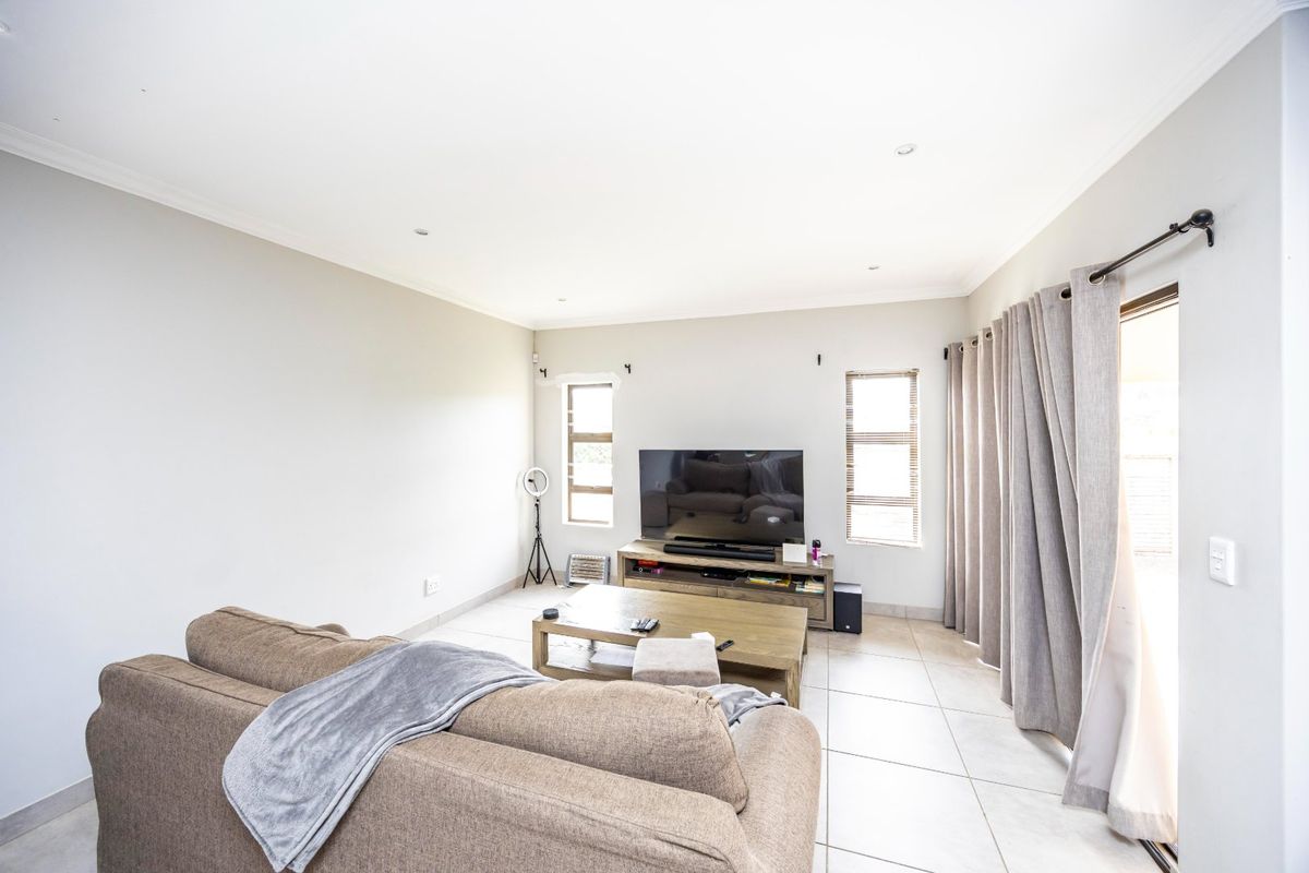 A bright and spacious living room featuring neutral tiled flooring, recessed downlighting, and a sliding glass door providing access to the outdoor area.