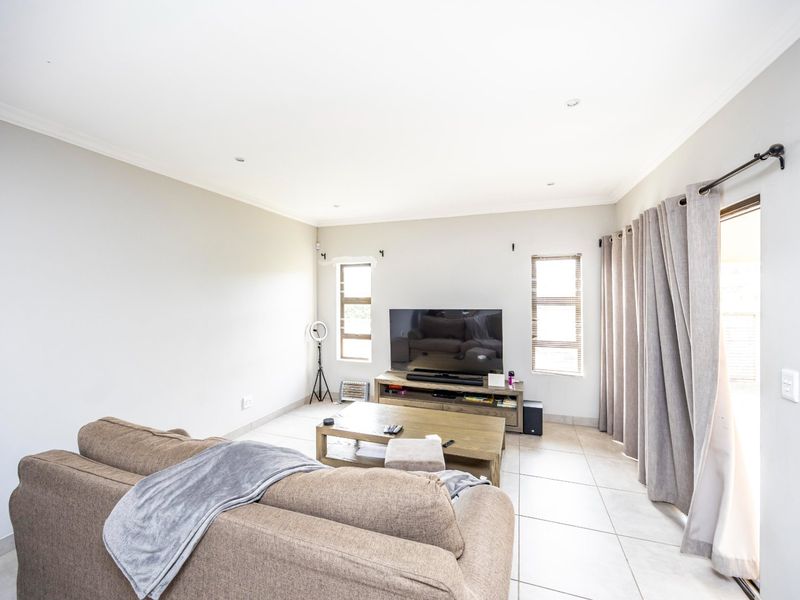 A bright and spacious living room featuring neutral tiled flooring, recessed downlighting, and a sliding glass door providing access to the outdoor area.