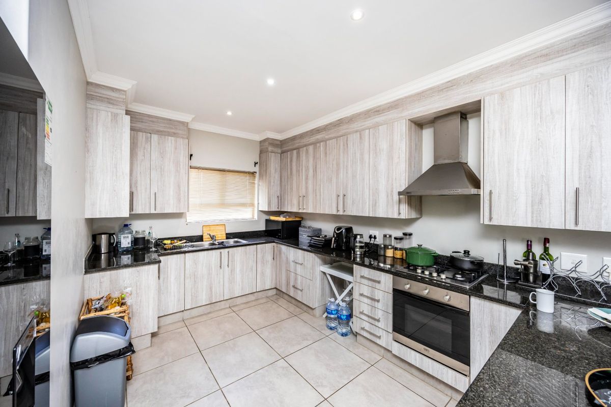 A well-maintained kitchen featuring light wood-grain cabinetry, granite countertops, a built-in oven with gas hob, and a stainless steel extractor fan.